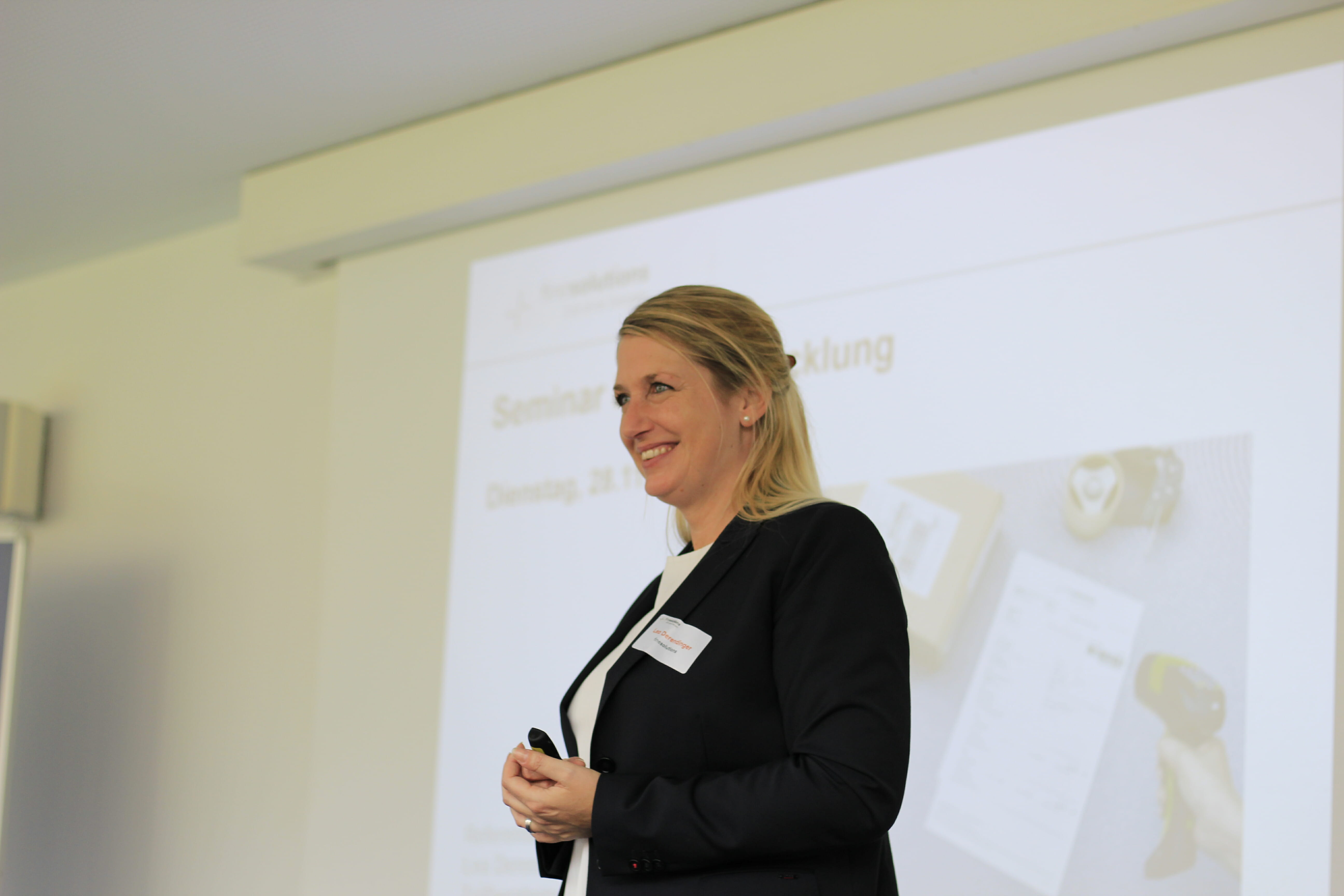 Lea Derendinger von FineSolutions steht vor einer Leinwand und hört Teilnehmern eines Zollseminars zu