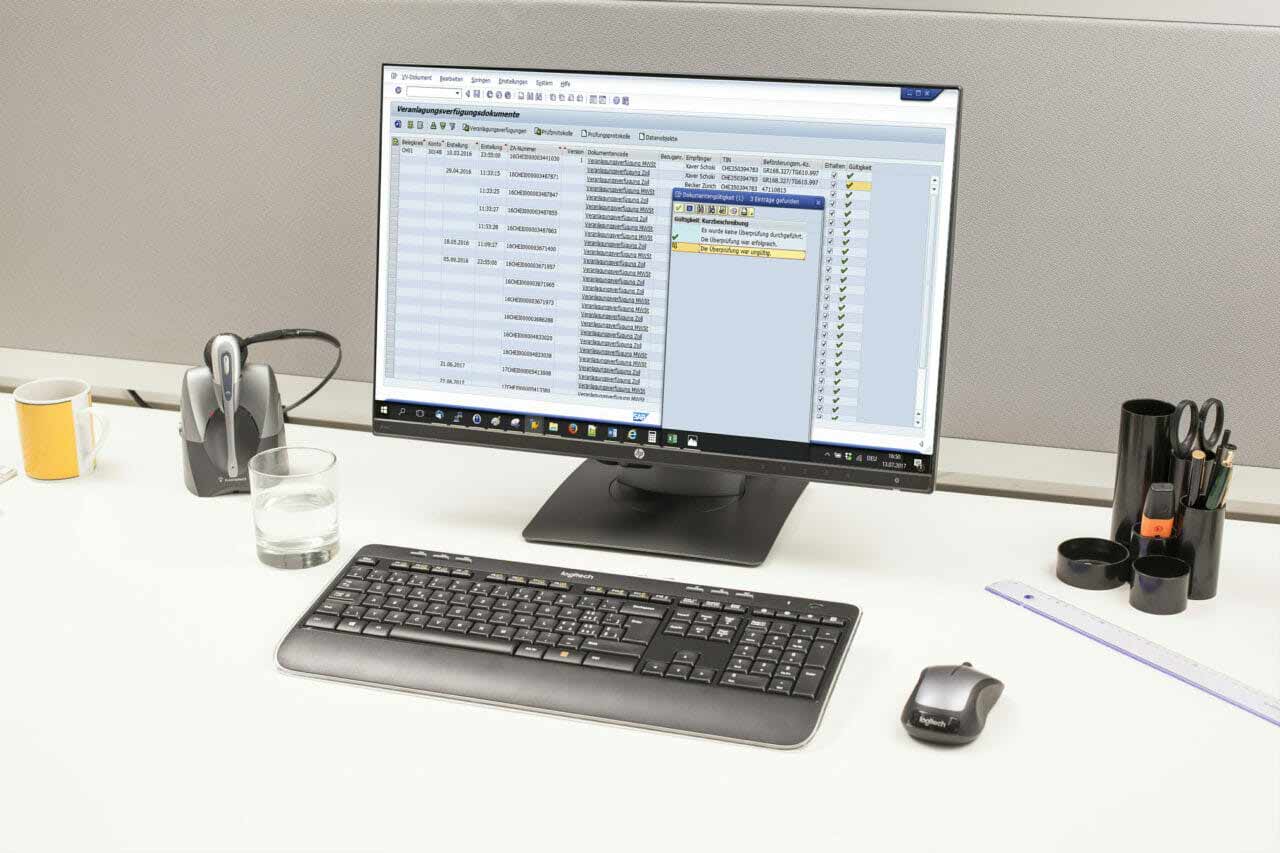 Anzeige der SAP-Zollsoftware auf Computerbildschirm auf einem Tisch mit Headset und Schreibzeug