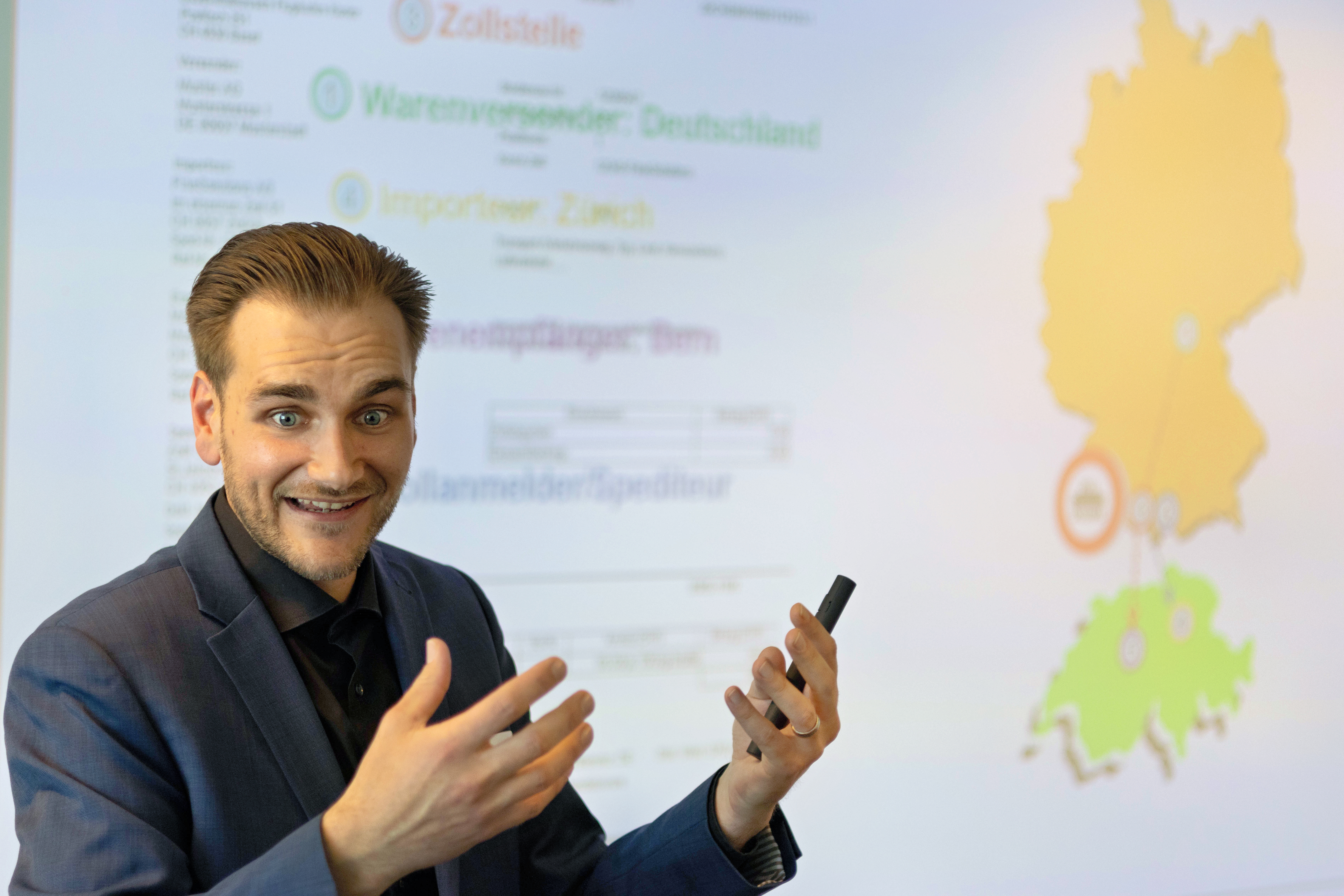 Fabian Mäder von FineSolutions steht als Zoll Seminarleiter vor der Folie und erklärt, auch mit Händen