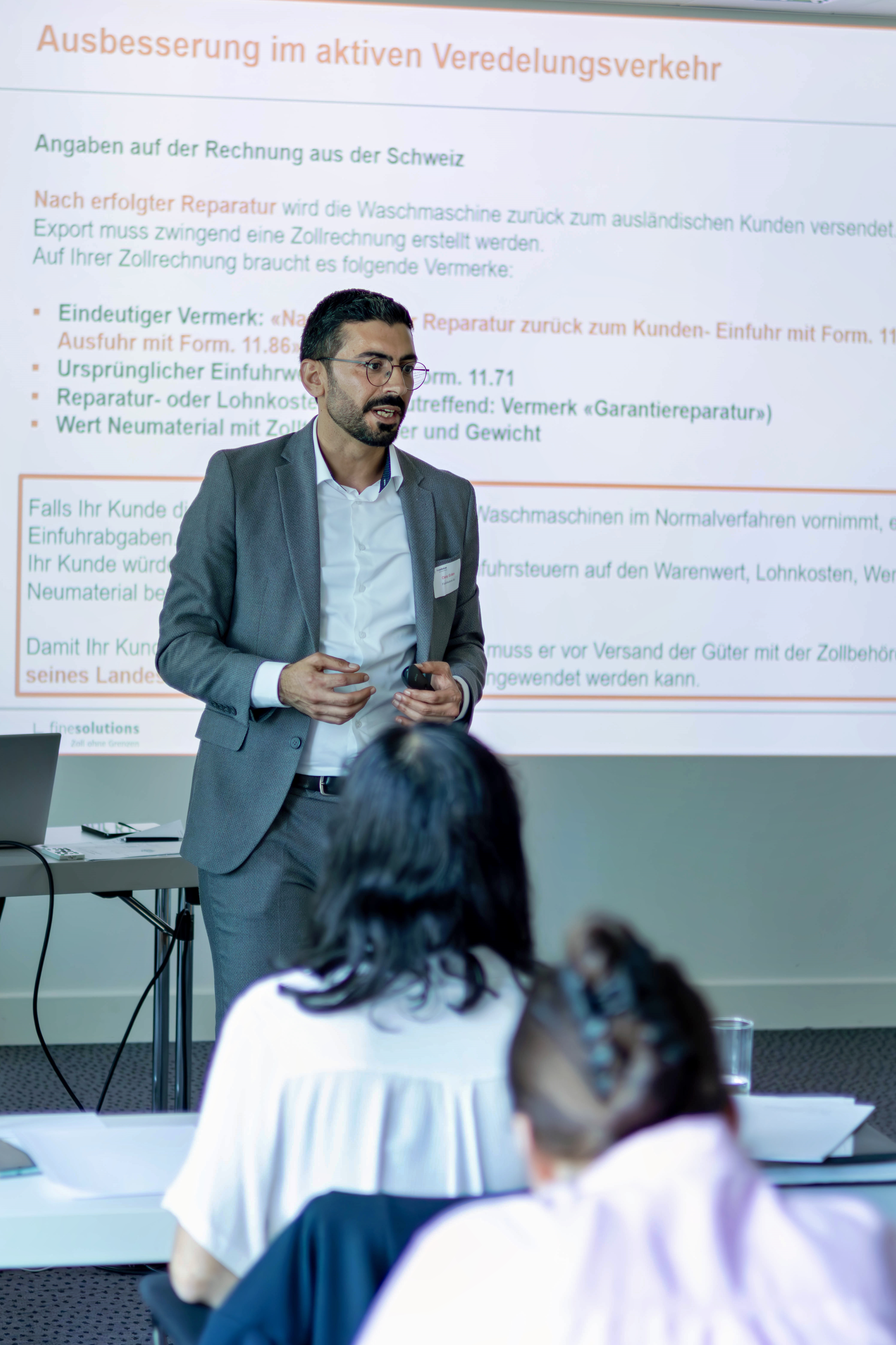Olcay Erden von FineSolutions steht als Zoll Seminarleiter im Seminarraum vor der Folie und den Teilnehmenden und spricht