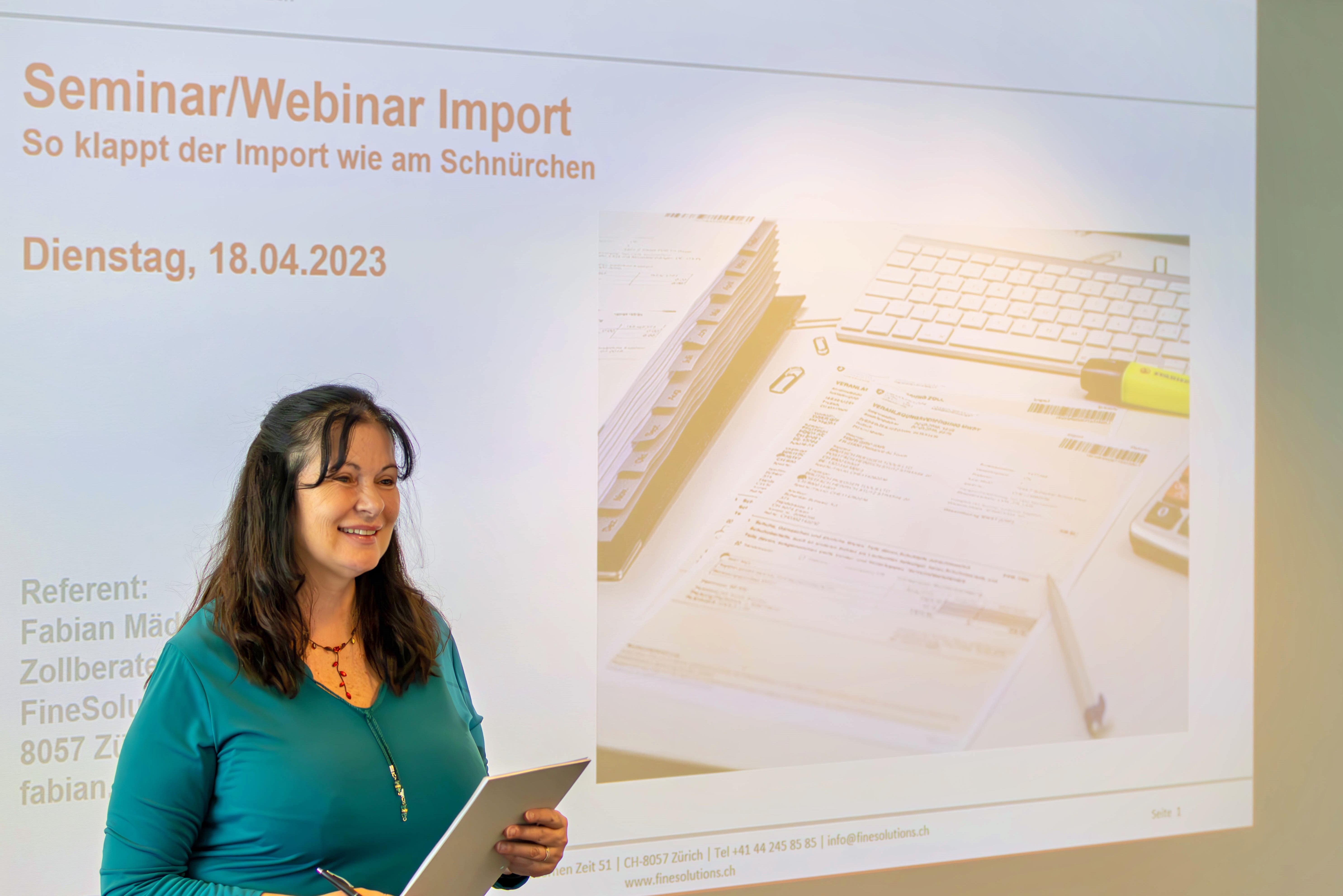 Simone Meier steht vor der Leinwand und begrüsst die Teilnehmenden an einem Zollseminar von FineSolutions