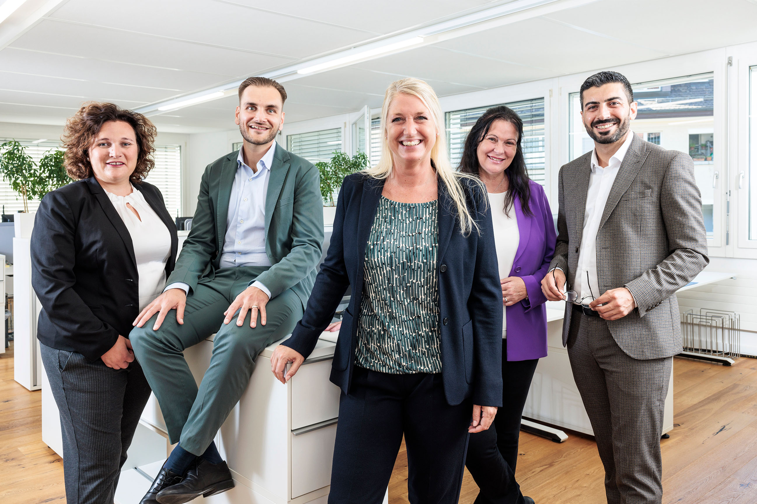 5 Personen stehend im Büro strahlend in die Kamera blickend